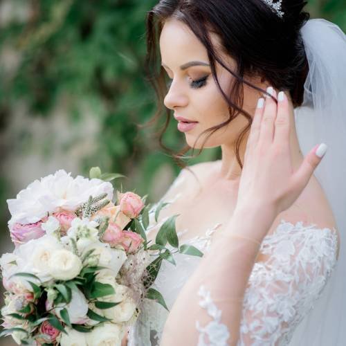 Attractive bride in crown with beautiful wedding bouquet made of white eustomas and pink roses